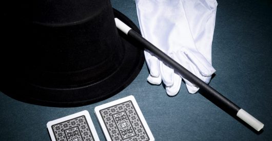 panoramic-view-playing-card-white-gloves-top-hat-magic-wand-green-background-min